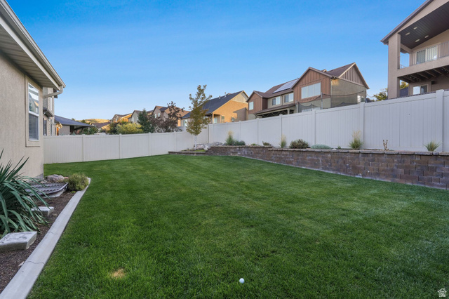 14738 Tangle Hill Road Herriman, UT 84096 - Photo 65 of 66 Expansive lawn area featuring a white privacy fence, decorative retaining wall with plantings, and concrete curbing