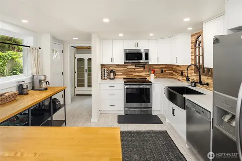 a kitchen with stainless steel appliances kitchen island granite countertop a stove top oven a sink dishwasher a refrigerator and white cabinets with wooden floor