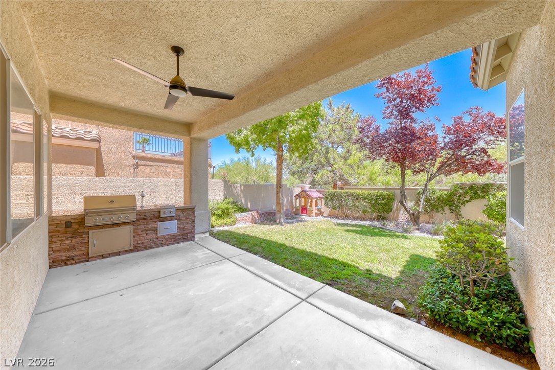 2122 Mooreview Street Henderson, NV 89012 - Photo 40 of 44 An inviting covered patio featuring a built-in barbecue and a ceiling fan overlooks a verdant, fenced backyard.