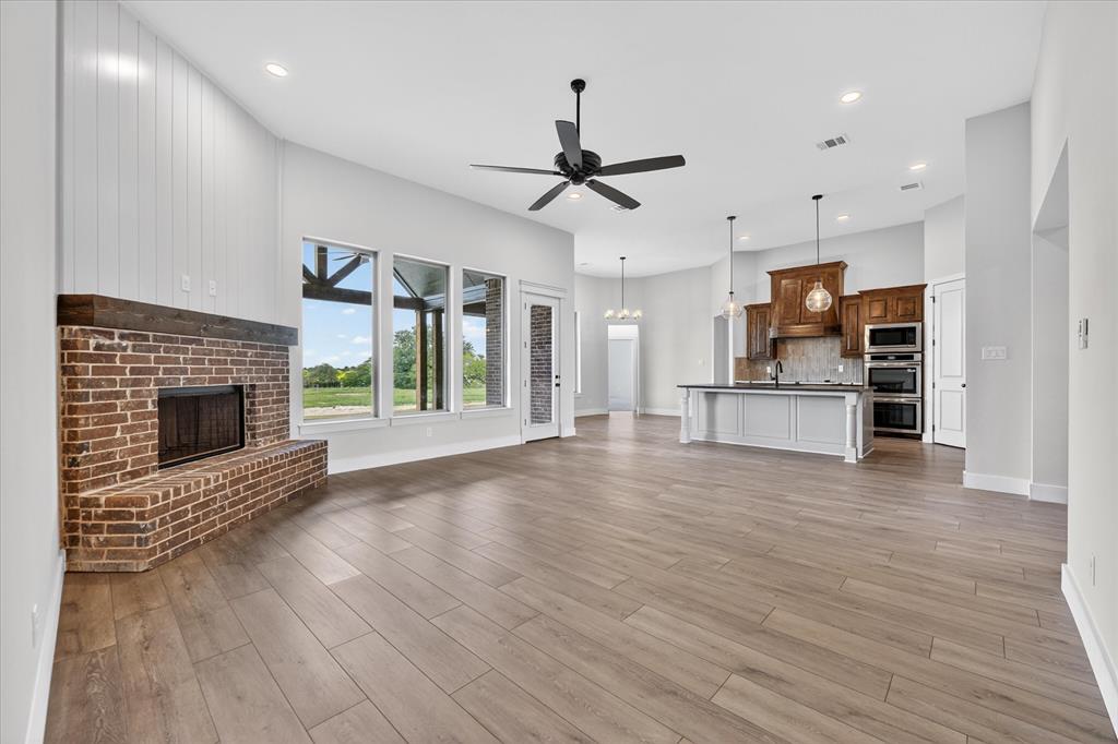 517 Longhorn Lane Springtown, TX 76082 - Photo 15 of 39 Unfurnished living room featuring a fireplace, a ceiling fan, light wood-style floors, and suspended lighting