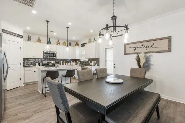 a kitchen with stainless steel appliances kitchen island granite countertop a refrigerator a stove a sink and white cabinets with wooden floor