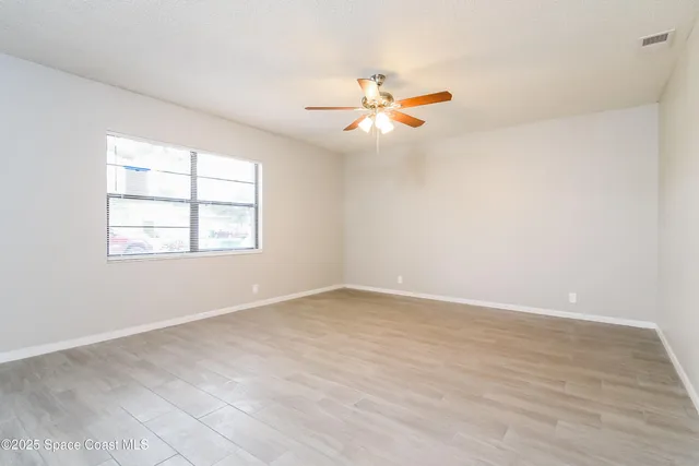 an empty room with wooden floor fan and windows