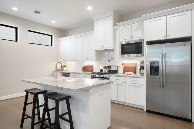 a kitchen with stainless steel appliances granite countertop a sink a stove a refrigerator cabinets and a dining table