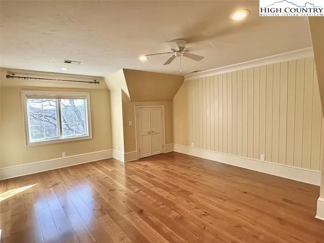 an empty room with wooden floor chandelier fan and windows