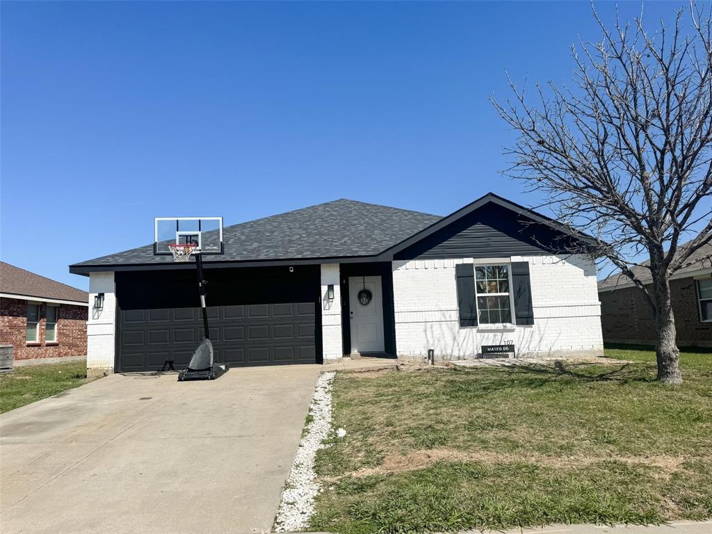 Single story home featuring a front yard, a garage, concrete driveway, brick siding, and roof with shingles