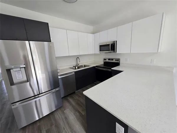 a kitchen with stainless steel appliances a refrigerator a stove a sink and white cabinets with wooden floor