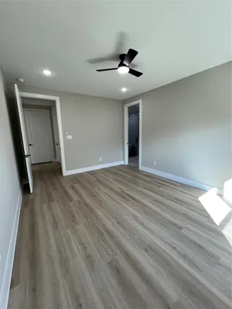 a view of an empty room with wooden floor and a ceiling fan