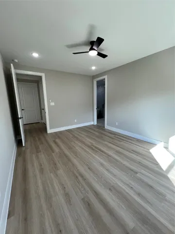 a view of an empty room with wooden floor and a ceiling fan