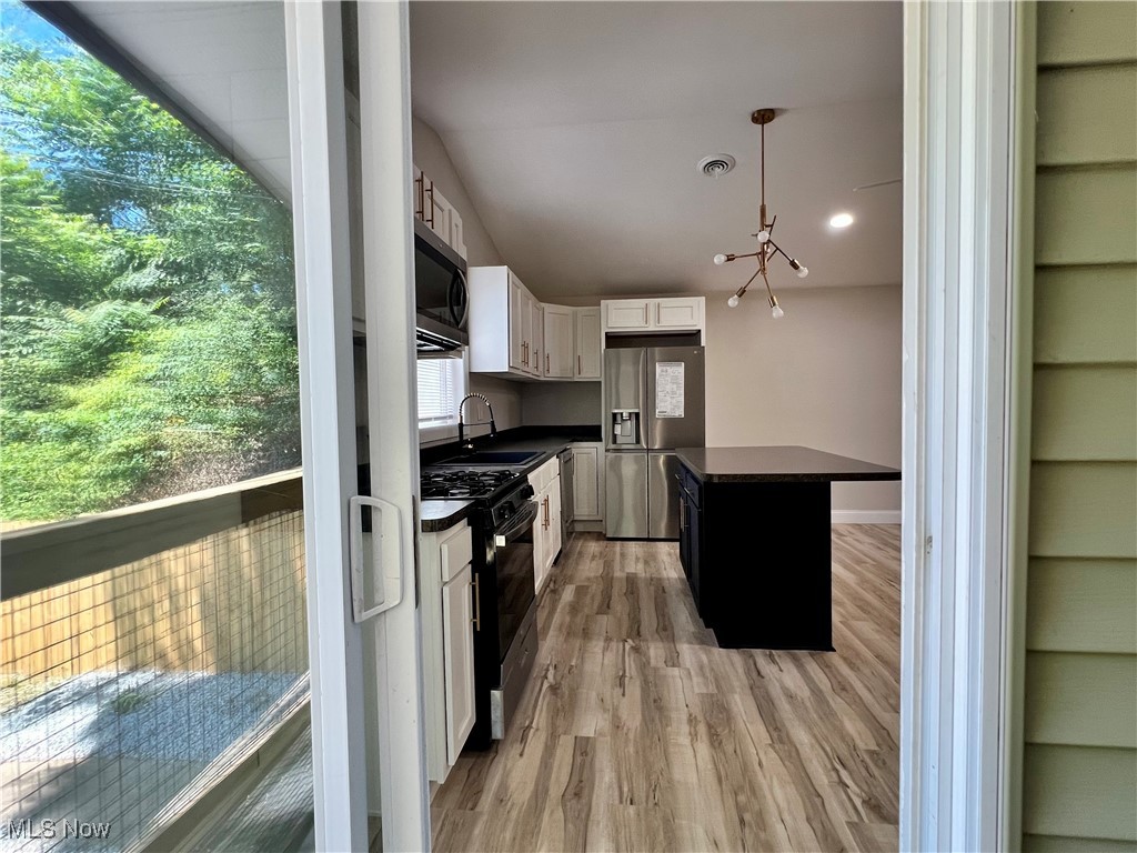 Kitchen with dark countertops, stainless steel appliances, white cabinetry, hanging light fixtures, and light wood-type flooring