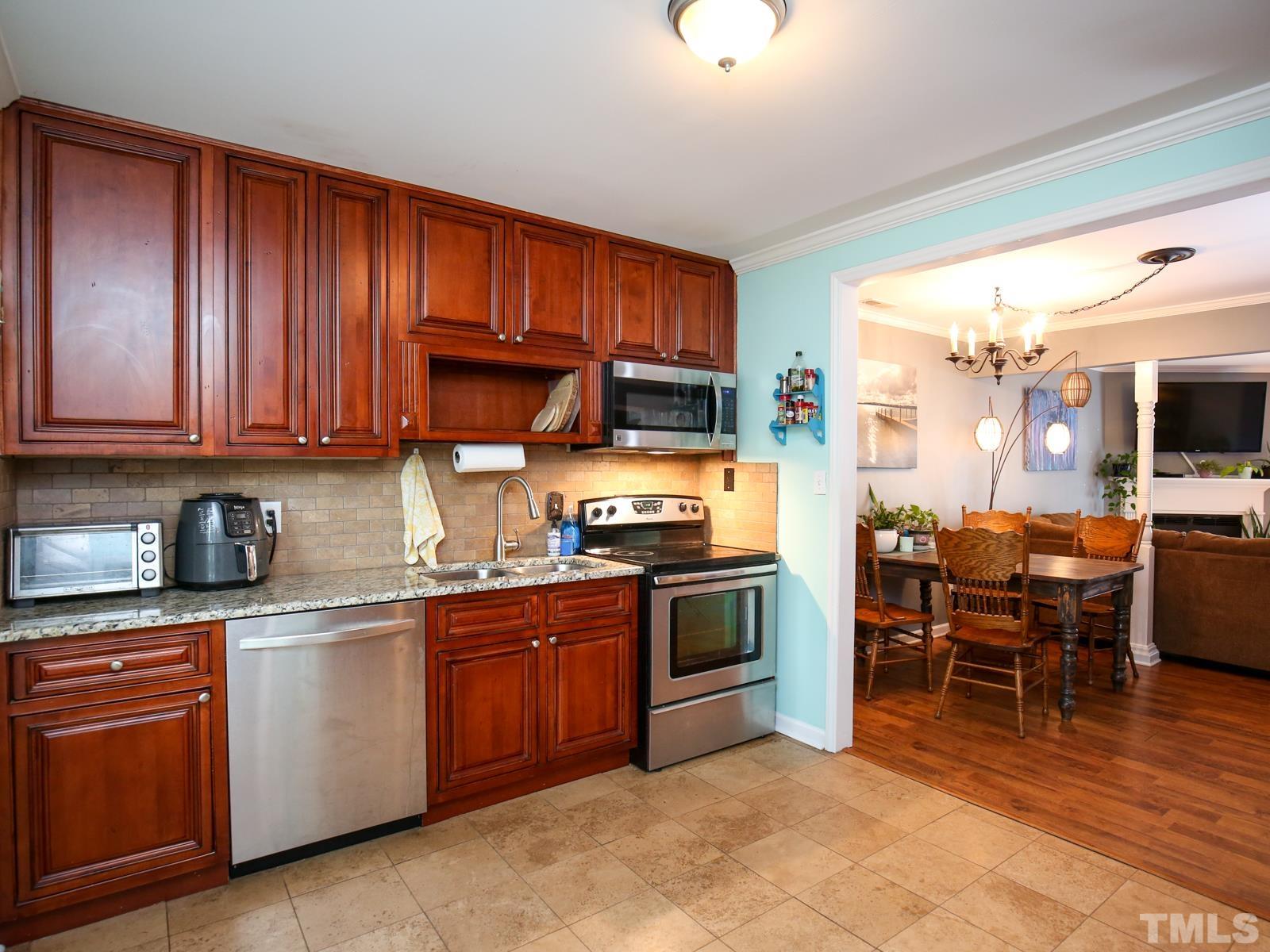 5423 Pine Top Circle Raleigh, NC 27612 - Photo 6 of 30 a kitchen with stainless steel appliances granite countertop a stove top oven a sink dishwasher a dining table and chairs with wooden floors