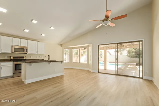 a open kitchen with granite countertop a stove top oven a sink and white cabinets with wooden floor