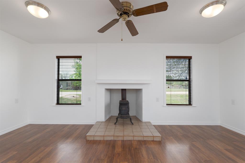 809 Turner Lane Tuscola, TX 79562 - Photo 16 of 25 Unfurnished living room with wood finished floors, a wood stove, and a ceiling fan
