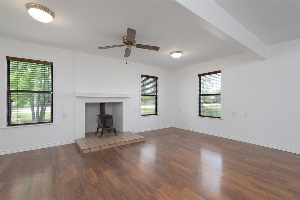 809 Turner Lane Tuscola, TX 79562 - Photo 18 of 25 Unfurnished living room featuring a wood stove, wood finished floors, and a ceiling fan