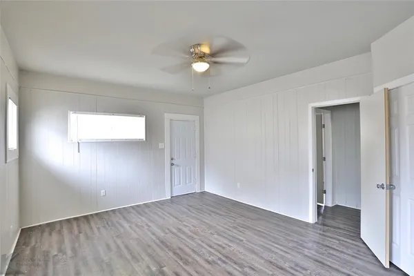 an empty room with wooden floor chandelier fan and windows