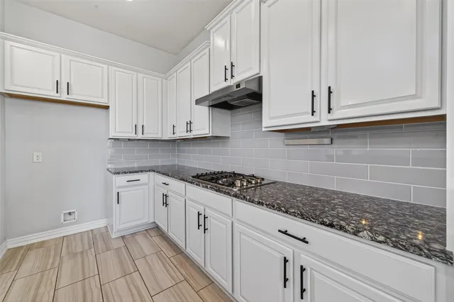 a kitchen with granite countertop a stove and white cabinets