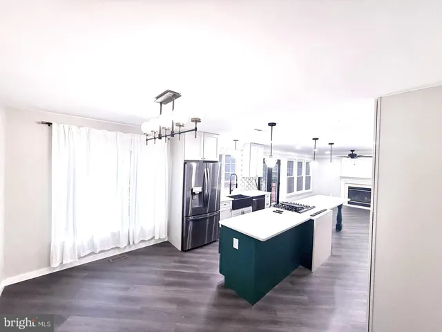 a living room with stainless steel appliances kitchen island granite countertop a refrigerator and a wooden floors