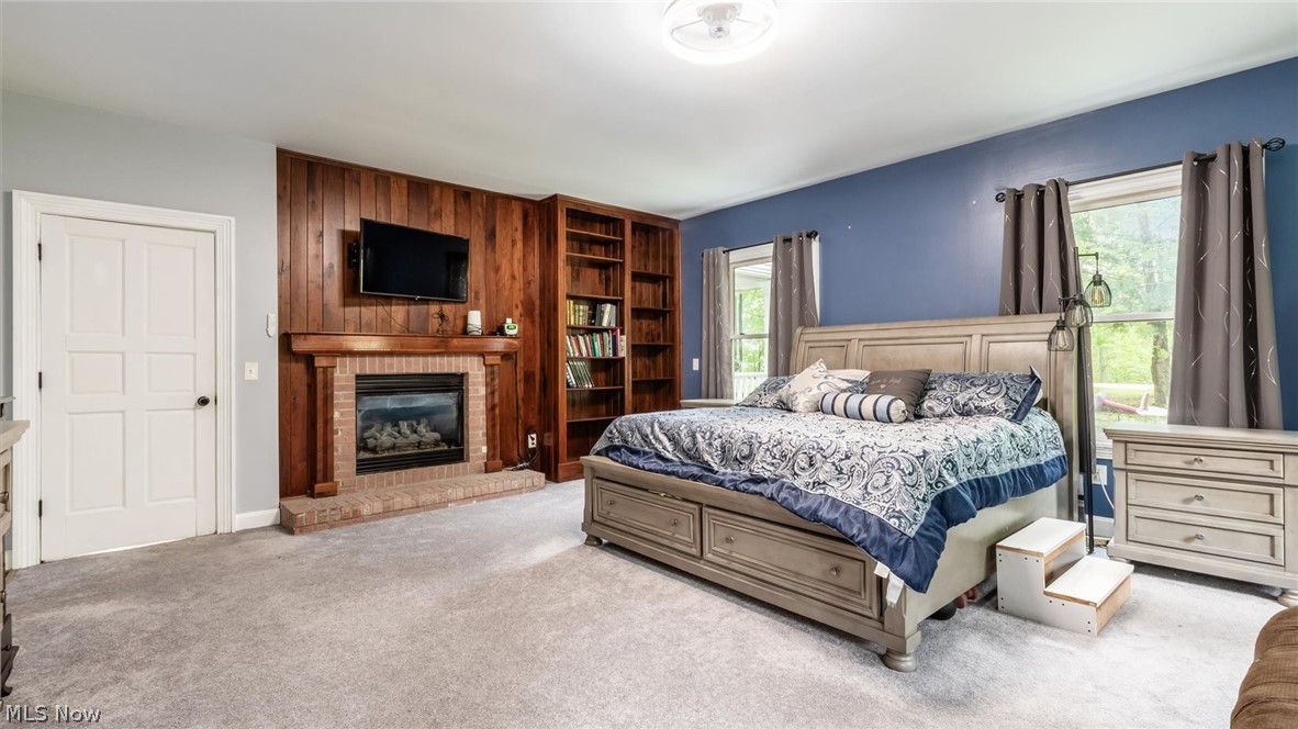 2531 Nicholas Lane Dresden, OH 43821 - Photo 13 of 40 Carpeted interior space featuring a brick fireplace with wood mantel, wood paneling, built-in shelving, two windows, and a ceiling fan