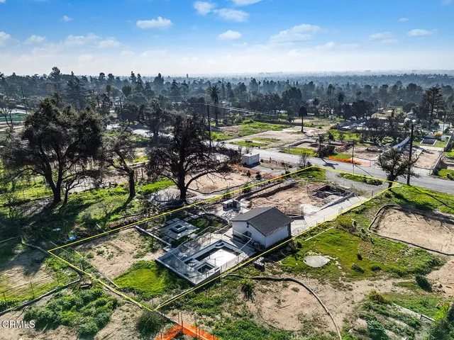 an aerial view of a residential houses with outdoor space and trees all around