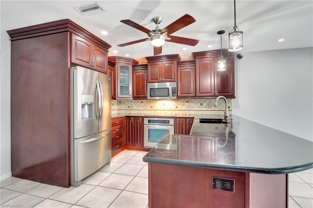 3035 42nd Terrace Southwest Naples, FL 34116 - Photo 18 of 48 Kitchen featuring stainless steel appliances, bold wood finish cabinetry, pendant lighting, a peninsula, and dark stone counters.