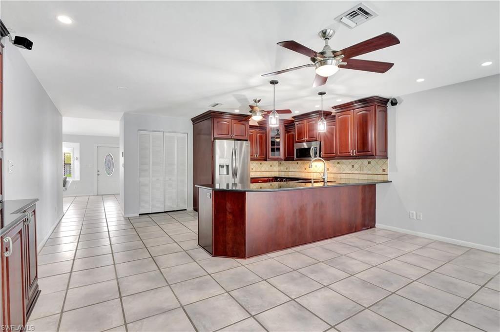 3035 42nd Terrace Southwest Naples, FL 34116 - Photo 19 of 48 Kitchen featuring wood finish cabinetry, a peninsula, stainless steel appliances, dark stone counters, and decorative backsplash.