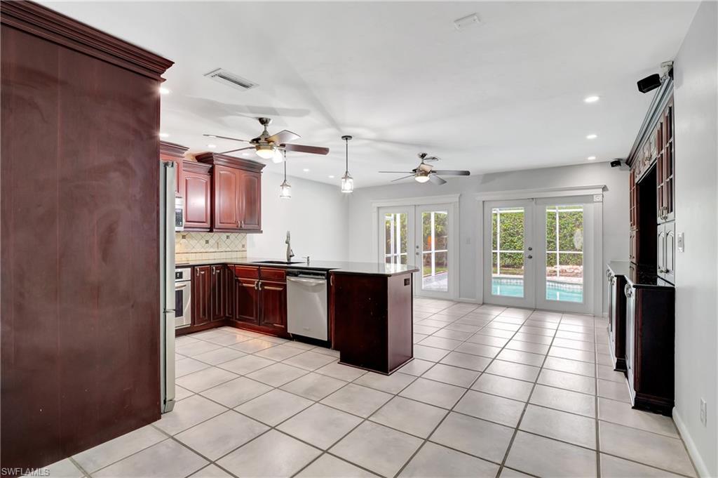 3035 42nd Terrace Southwest Naples, FL 34116 - Photo 21 of 48 Kitchen with French doors, wood finish cabinets, a peninsula, decorative backsplash, and stainless steel appliances.