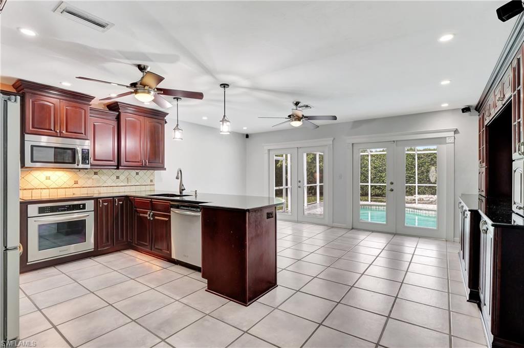 3035 42nd Terrace Southwest Naples, FL 34116 - Photo 30 of 48 Kitchen with french doors, wood finish cabinets, hanging light fixtures, stainless steel appliances, and decorative backsplash.