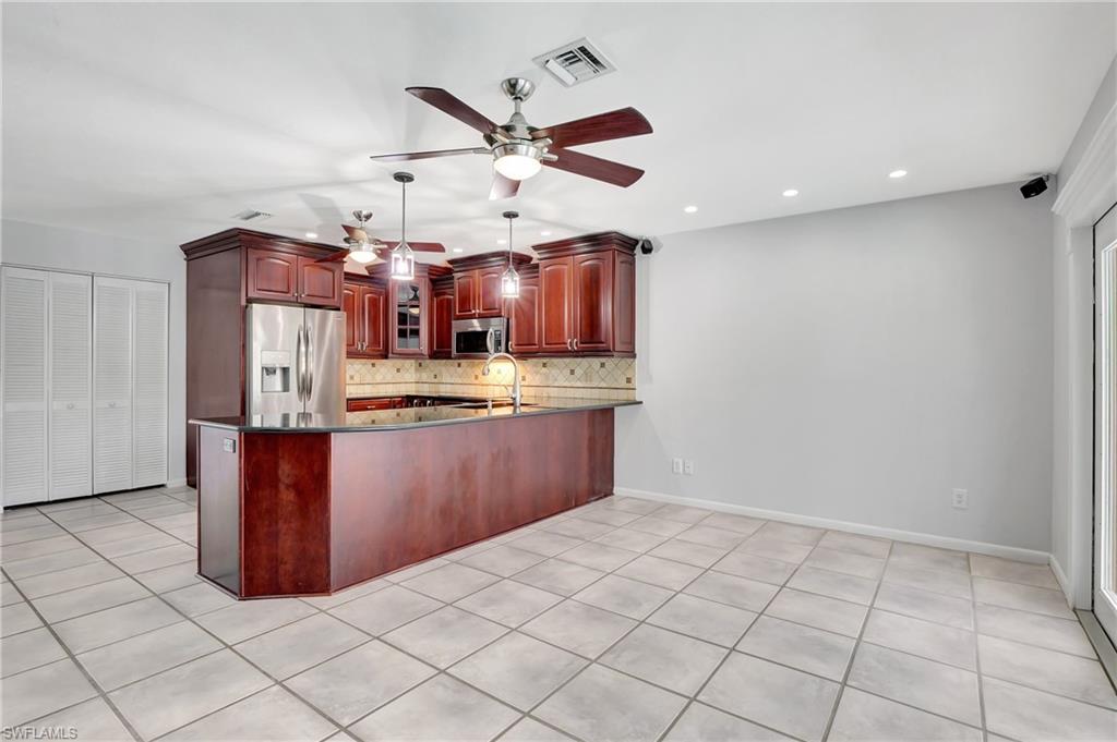 3035 42nd Terrace Southwest Naples, FL 34116 - Photo 33 of 48 Kitchen featuring cherry color cabinets, stainless steel appliances, a peninsula, dark stone countertops, and decorative backsplash