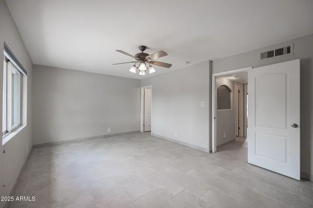 an empty room with chandelier fan and windows