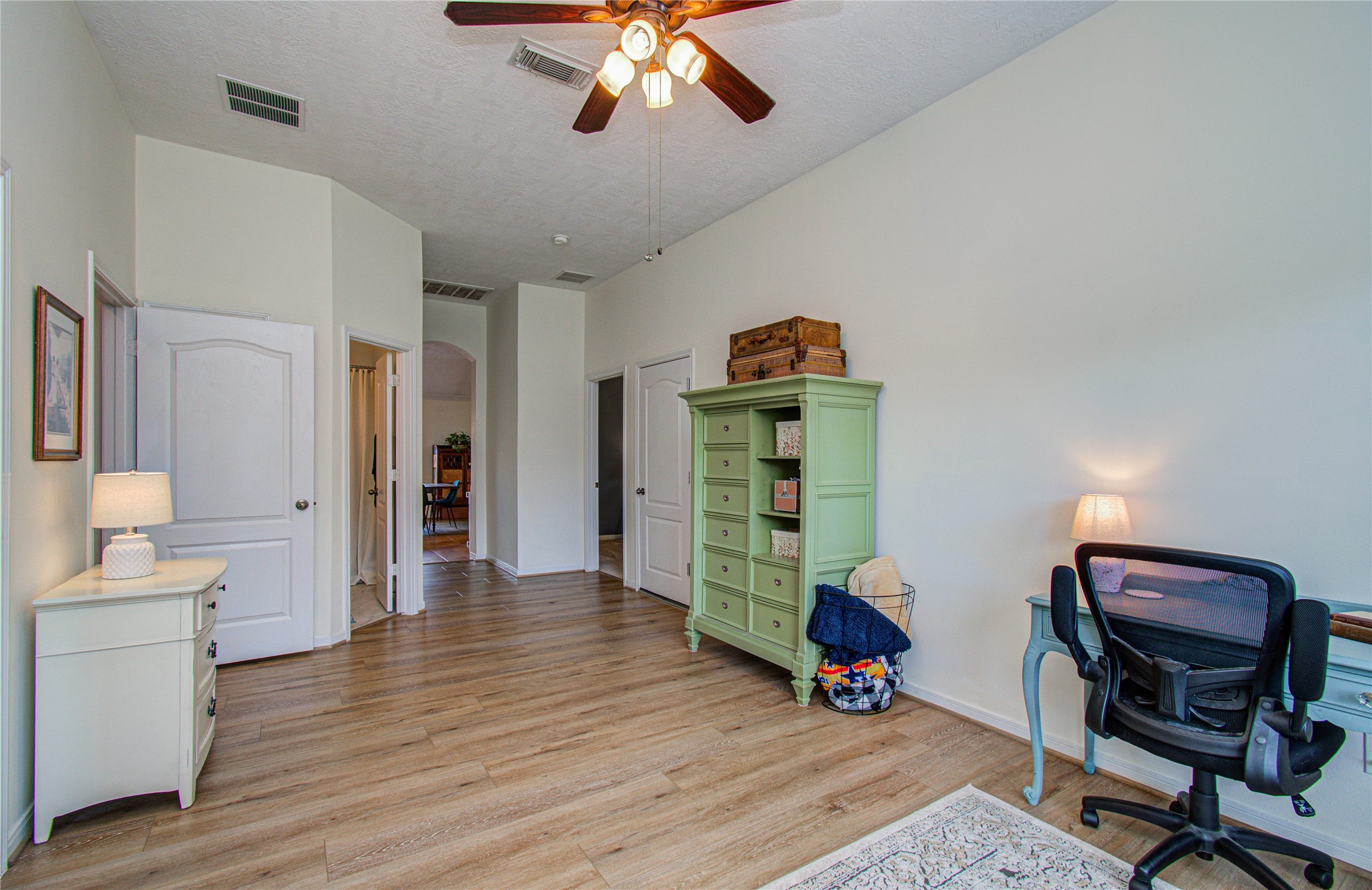 20007 Alcea Court Spring, TX 77379 - Photo 21 of 36 This room features a bright, spacious layout with light wood flooring and neutral walls. It includes a ceiling fan, a desk with a chair, and ample storage with a green dresser. Perfect for a home office or study area.
