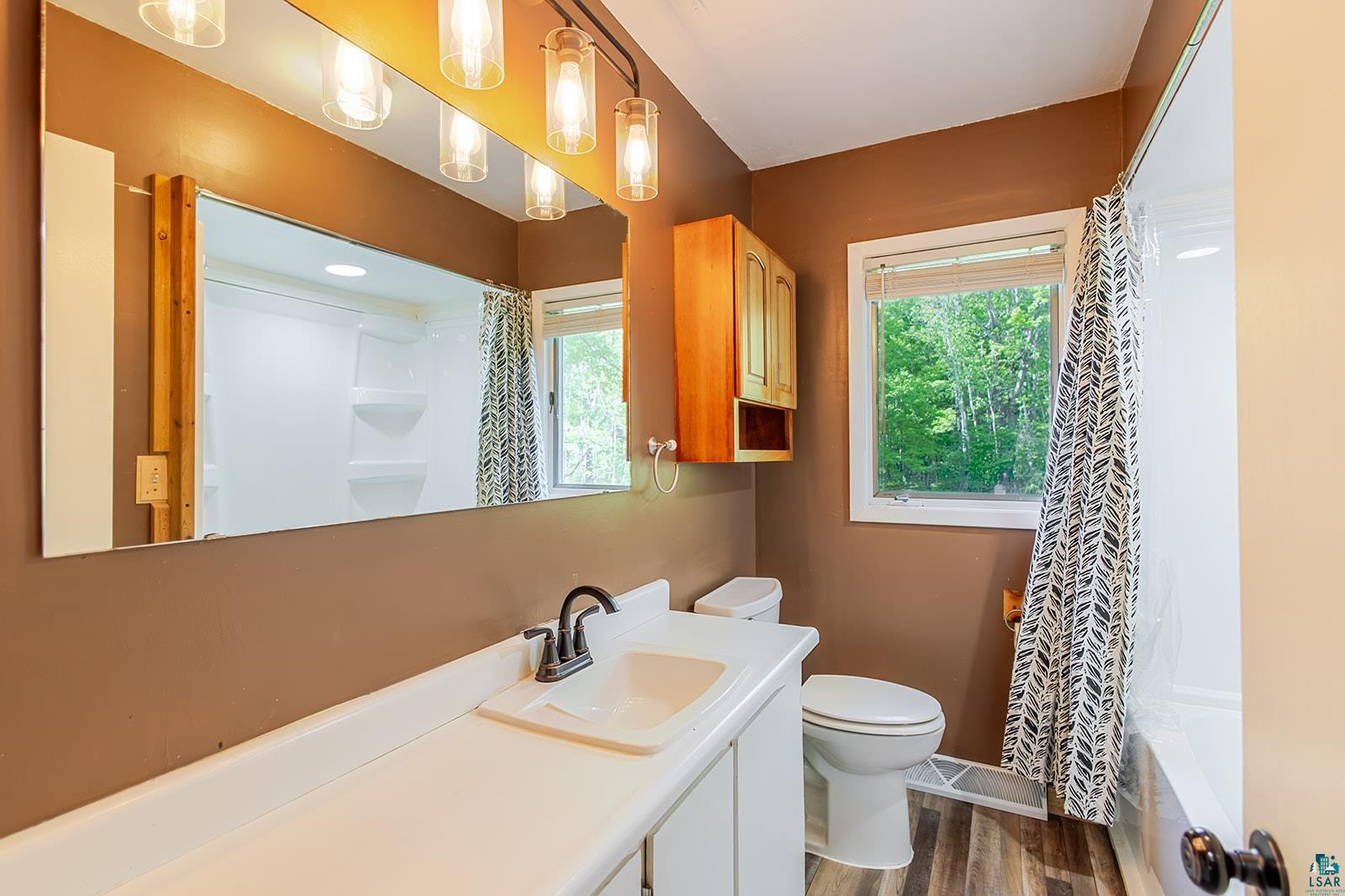 7045 Morris Thomas Road Cloquet, MN 55720 - Photo 14 of 28 Bathroom featuring a single vanity with an integrated sink, wood-finish flooring, a window providing natural light, a built-in wooden cabinet, and a shower-tub combination