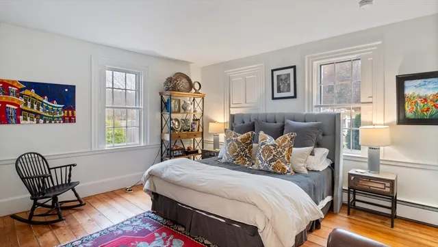 a bedroom with a bed chair and two windows