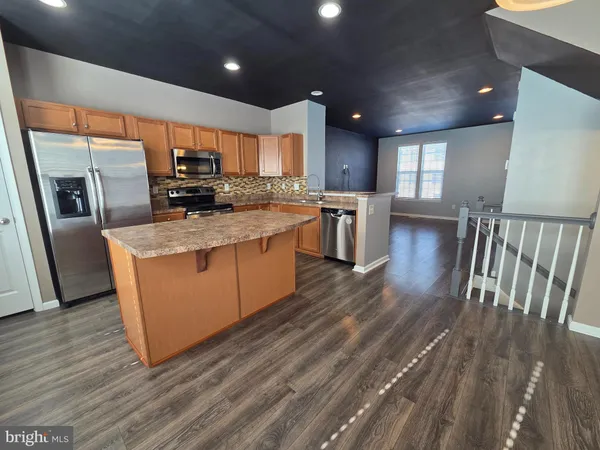 a kitchen with stainless steel appliances granite countertop a refrigerator a sink dishwasher a stove and a oven with wooden floor