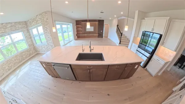 a kitchen with stainless steel appliances a dining table wooden floor a large window and white cabinets