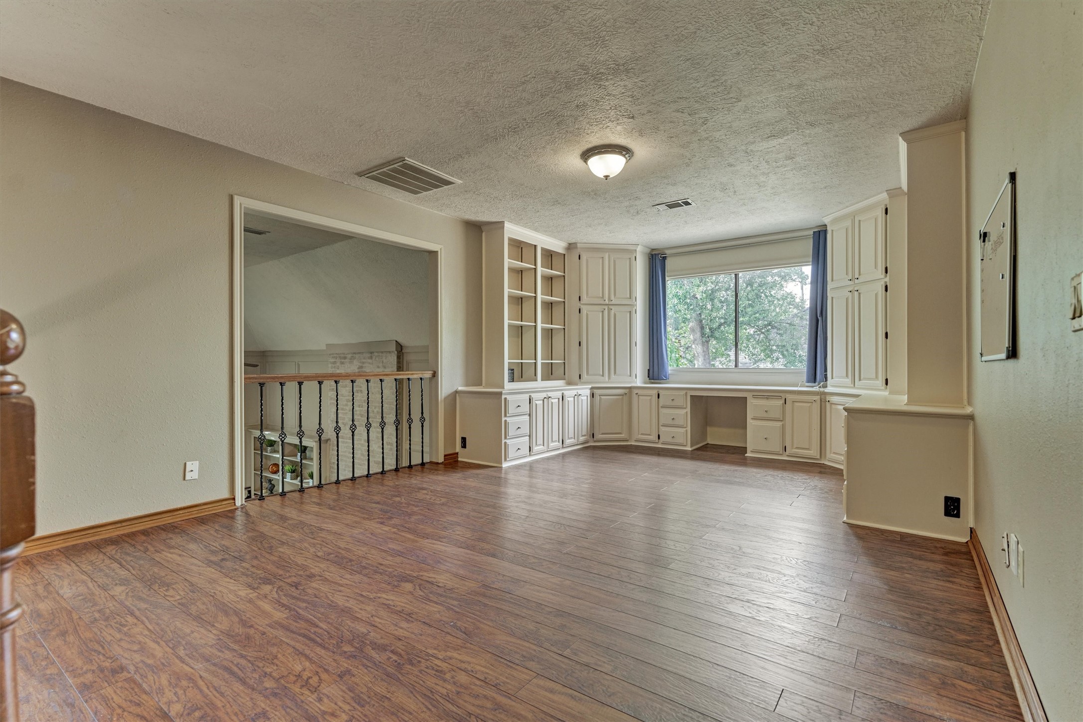 25706 Overlake Drive Spring, TX 77380 - Photo 23 of 32 This spacious game room features hardwood flooring, built-in shelves, and cabinets. A large window with a view provides natural light, and there's a convenient built-in desk area perfect for a home office or study. The open railing adds a touch of elegance to the space.