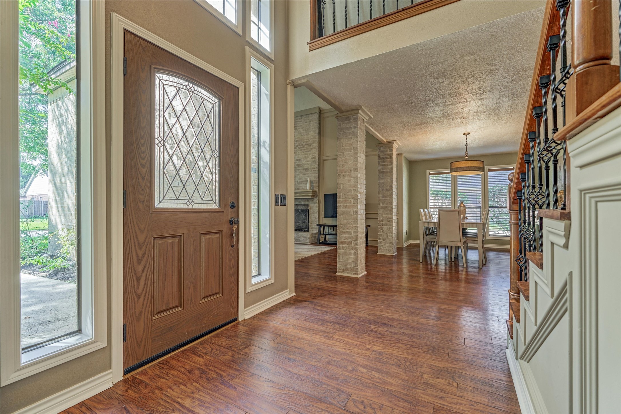 25706 Overlake Drive Spring, TX 77380 - Photo 32 of 32 This inviting entryway featuring high ceilings, and abundant natural light. The open floor plan reveals a spacious living area with hardwood floors and a view of the dining space, accented by elegant columns and a staircase with wrought iron details.