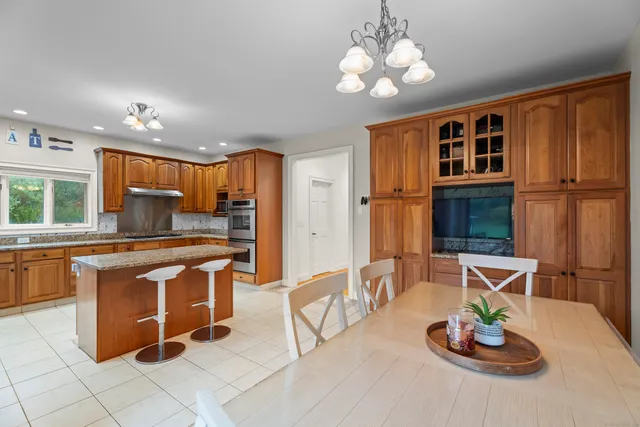 a kitchen with stainless steel appliances granite countertop a stove a refrigerator a sink a dining table and chairs with wooden floor