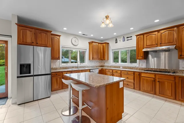 a kitchen with stainless steel appliances granite countertop a refrigerator a sink dishwasher a stove and white countertops with wooden cabinets