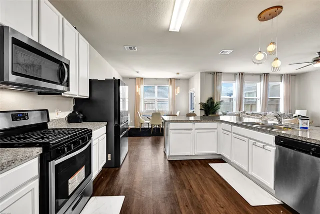 a kitchen with stainless steel appliances a microwave a stove a sink dishwasher a refrigerator and white cabinets with wooden floor