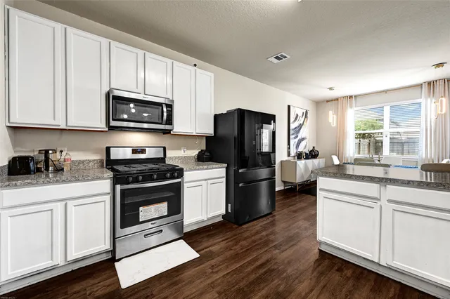 a kitchen with stainless steel appliances granite countertop a stove a sink dishwasher a refrigerator and a microwave oven with wooden floor