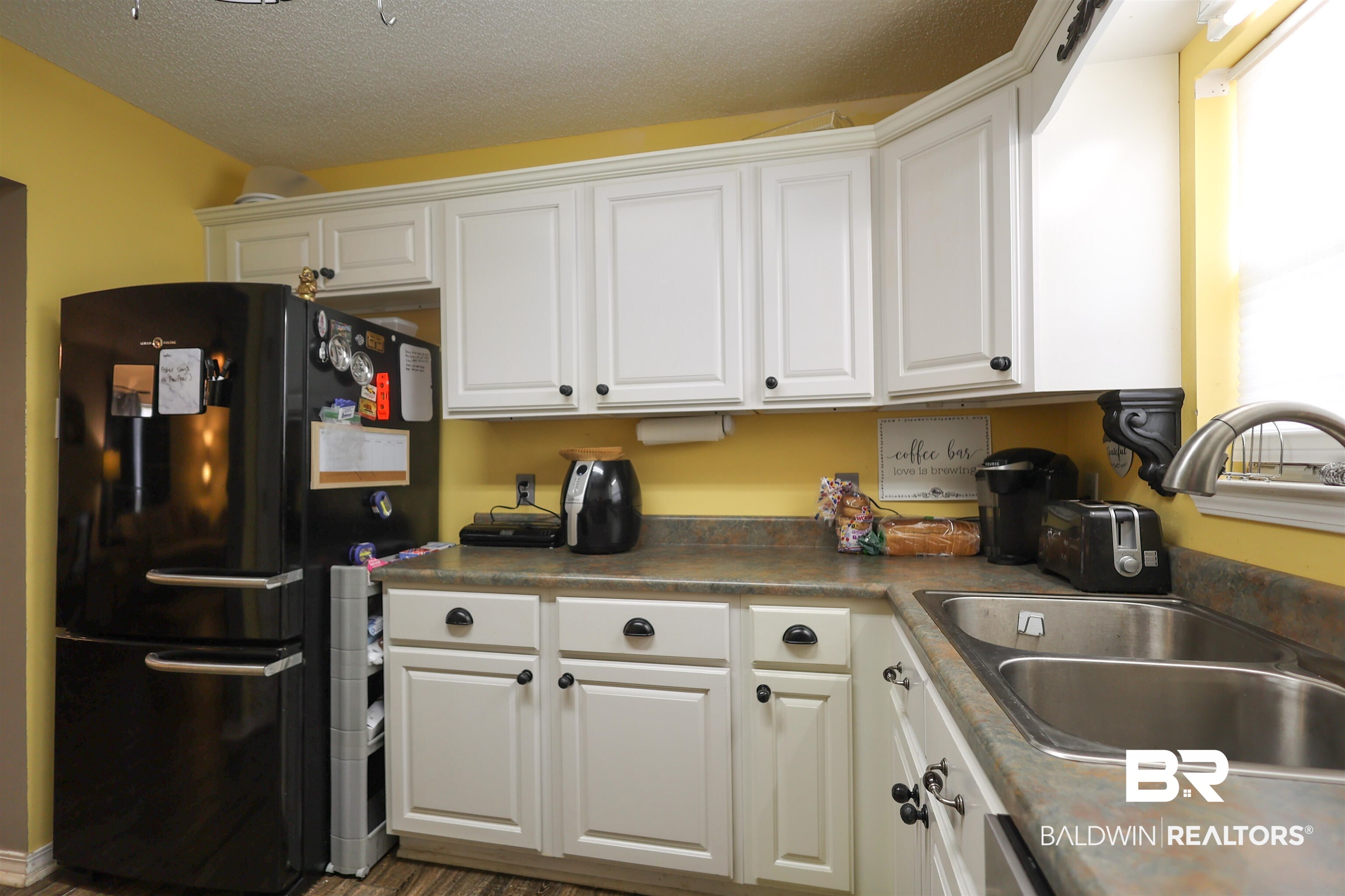 7790 Audubon Drive Foley, AL 36535 - Photo 11 of 39 Kitchen featuring white cabinetry with black hardware, a stainless steel double sink, and solid surface countertops