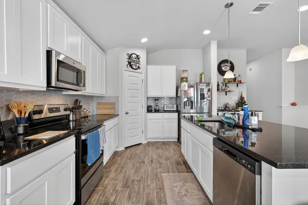 a kitchen with stainless steel appliances granite countertop a refrigerator a stove top oven a sink dishwasher a dining table and chairs with wooden floor
