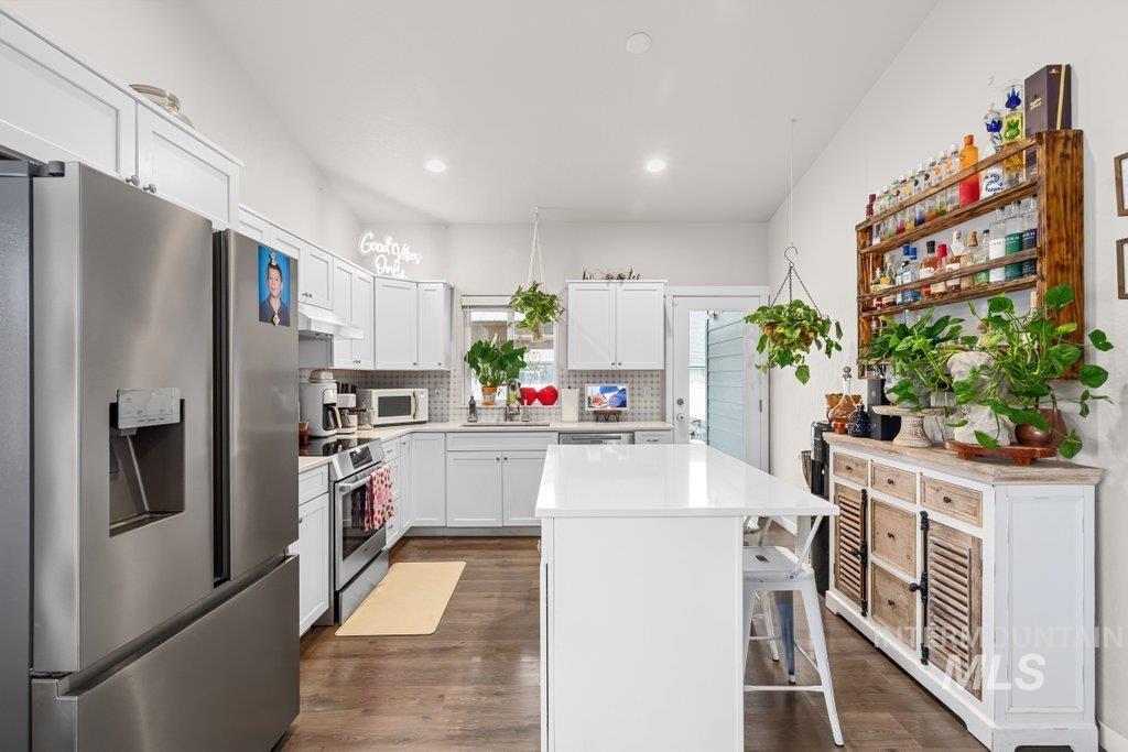 6697 West Irish Circle Rathdrum, ID 83858 - Photo 7 of 36 Kitchen featuring stainless steel appliances, dark wood-style flooring, white cabinetry, a center island, and a kitchen bar