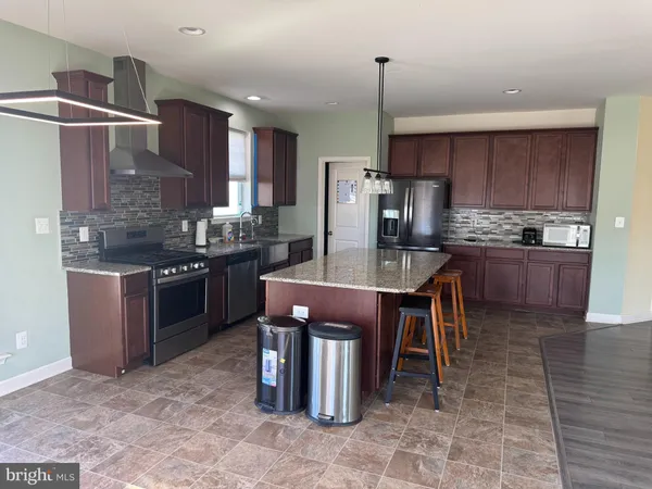 a kitchen with stainless steel appliances a sink a stove a refrigerator and chairs