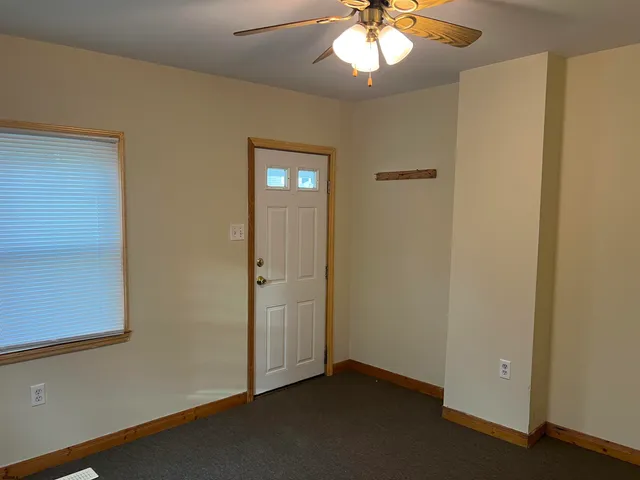 an empty room with a chandelier fan and wooden floor