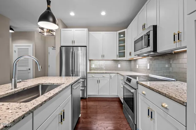 a kitchen with stainless steel appliances granite countertop a refrigerator a sink dishwasher a stove and white cabinets with wooden floor