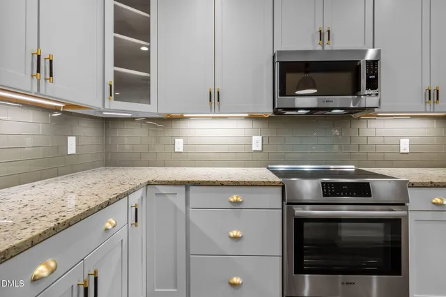 a kitchen with stainless steel appliances granite countertop a refrigerator a sink dishwasher a stove and white cabinets with wooden floor