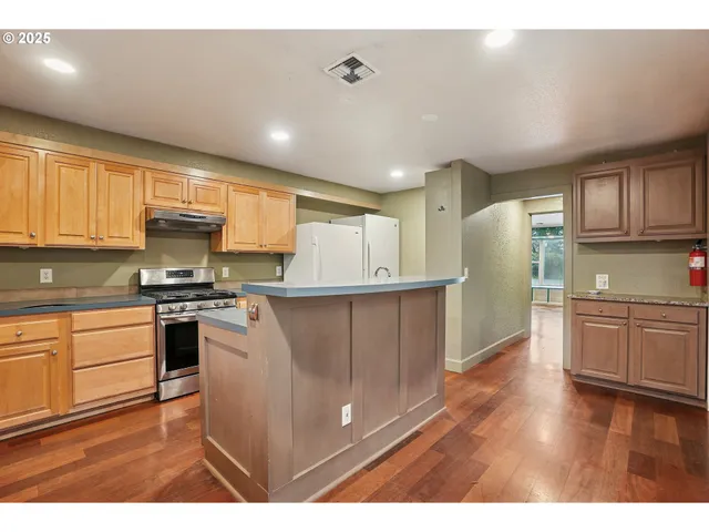 a kitchen with stainless steel appliances granite countertop a refrigerator a sink dishwasher a stove and white countertops with wooden floor