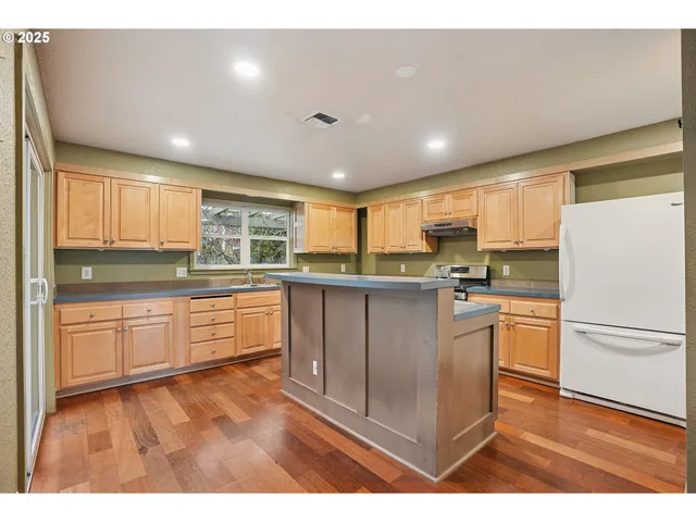 a kitchen with stainless steel appliances granite countertop a refrigerator a sink dishwasher a stove and white countertops with wooden floor