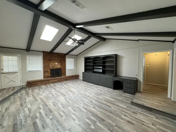 an empty room with wooden floor kitchen view and a window