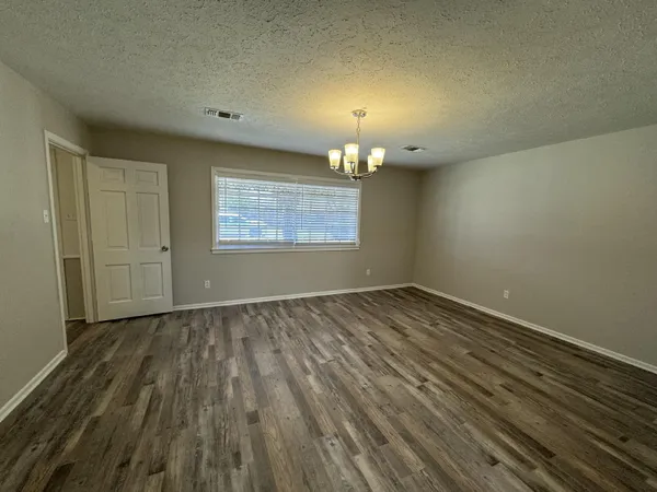 an empty room with wooden floor chandelier and windows